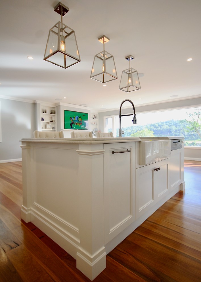 Inspiration for a large transitional l-shaped eat-in kitchen in Sydney with a farmhouse sink, recessed-panel cabinets, white cabinets, quartz benchtops, grey splashback, stone slab splashback, stainless steel appliances, medium hardwood floors, with island and brown floor.