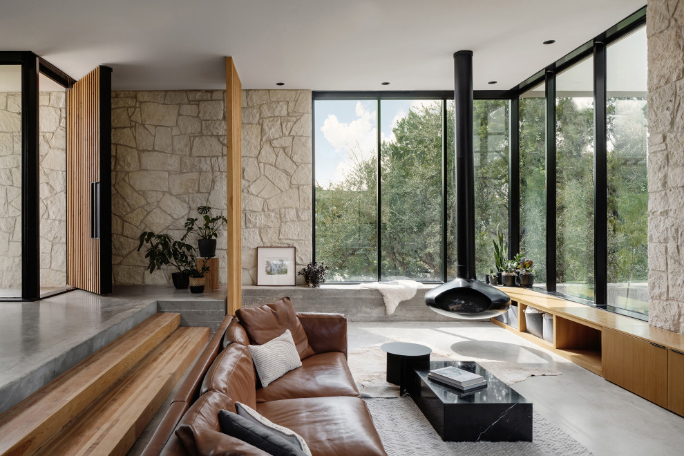Ejemplo de salón abierto minimalista de tamaño medio con suelo de cemento, chimeneas suspendidas y piedra