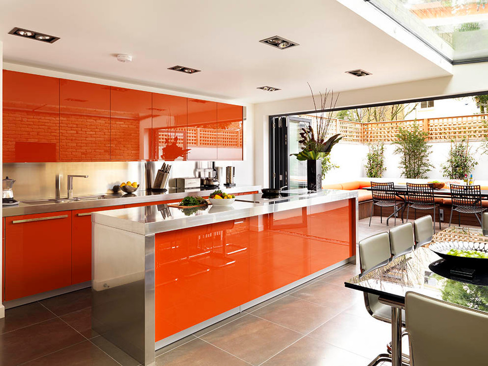 Contemporary galley eat-in kitchen in London with flat-panel cabinets, stainless steel benchtops, porcelain floors, with island and red cabinets.