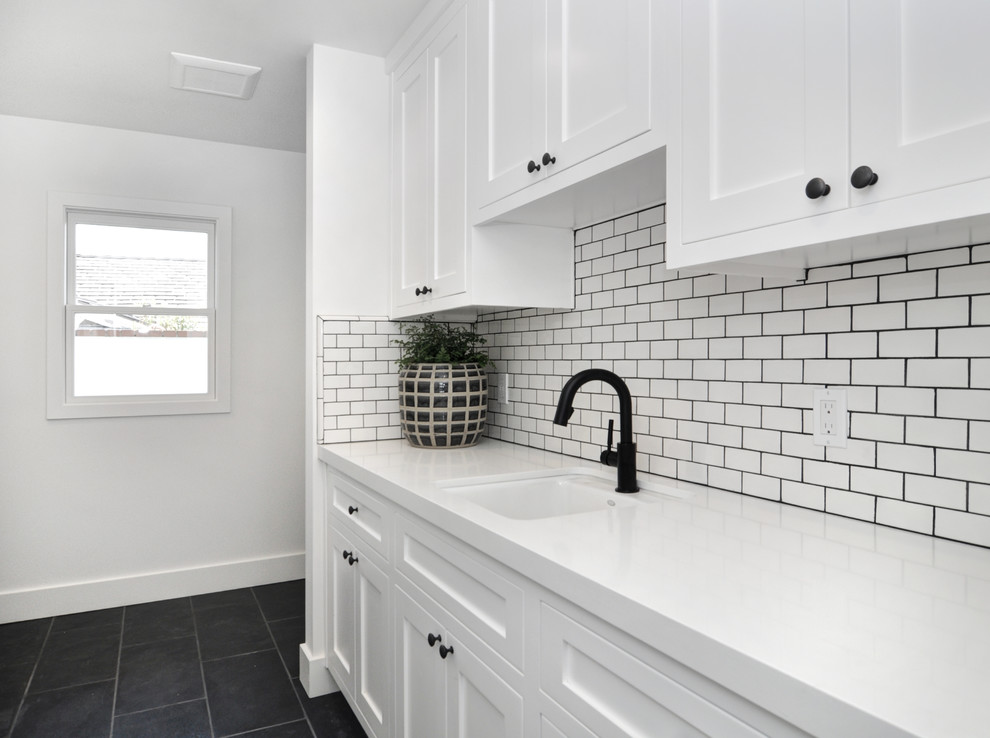 Mid-sized beach style single-wall dedicated laundry room in Orange County with an undermount sink, shaker cabinets, white cabinets, quartz benchtops, white walls, slate floors, black floor and white benchtop.