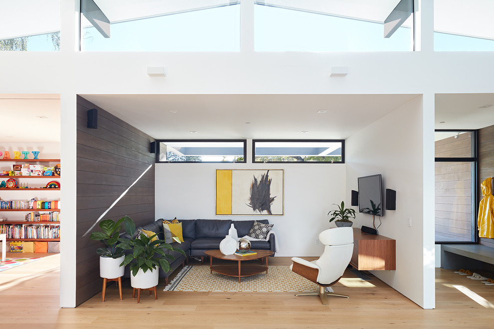 Midcentury open concept living room in San Francisco with white walls, light hardwood floors, no fireplace and a wall-mounted tv.