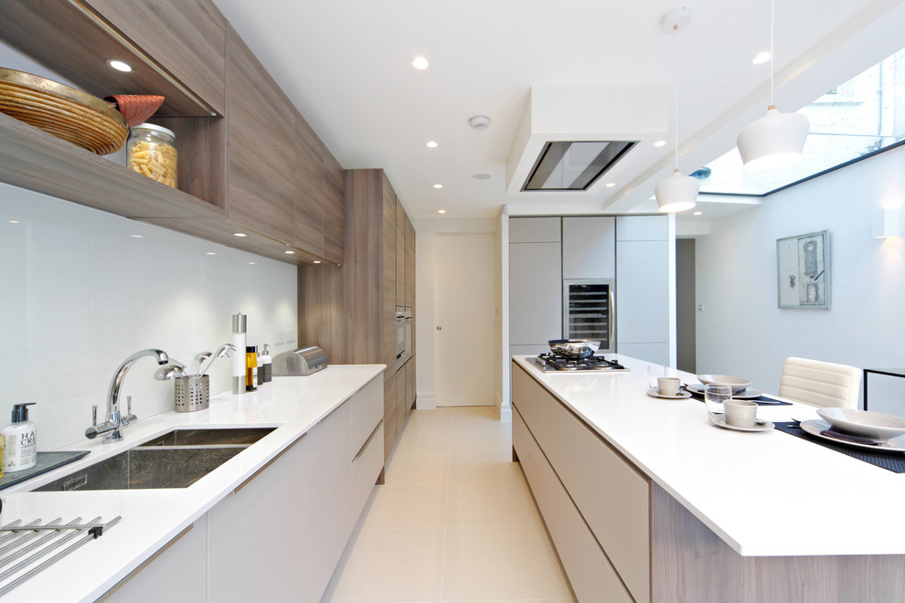 Large contemporary galley eat-in kitchen in London with an integrated sink, flat-panel cabinets, medium wood cabinets, quartz benchtops, grey splashback, glass sheet splashback, stainless steel appliances, ceramic floors and with island.
