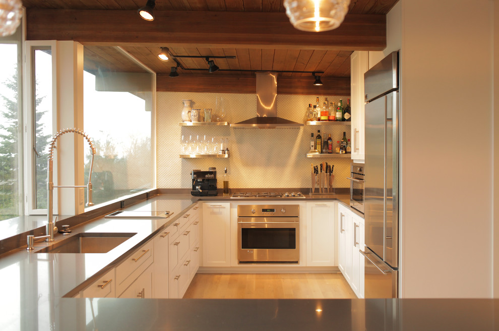 Small midcentury u-shaped open plan kitchen in Seattle with an undermount sink, shaker cabinets, white cabinets, quartz benchtops, grey splashback, stainless steel appliances and light hardwood floors.