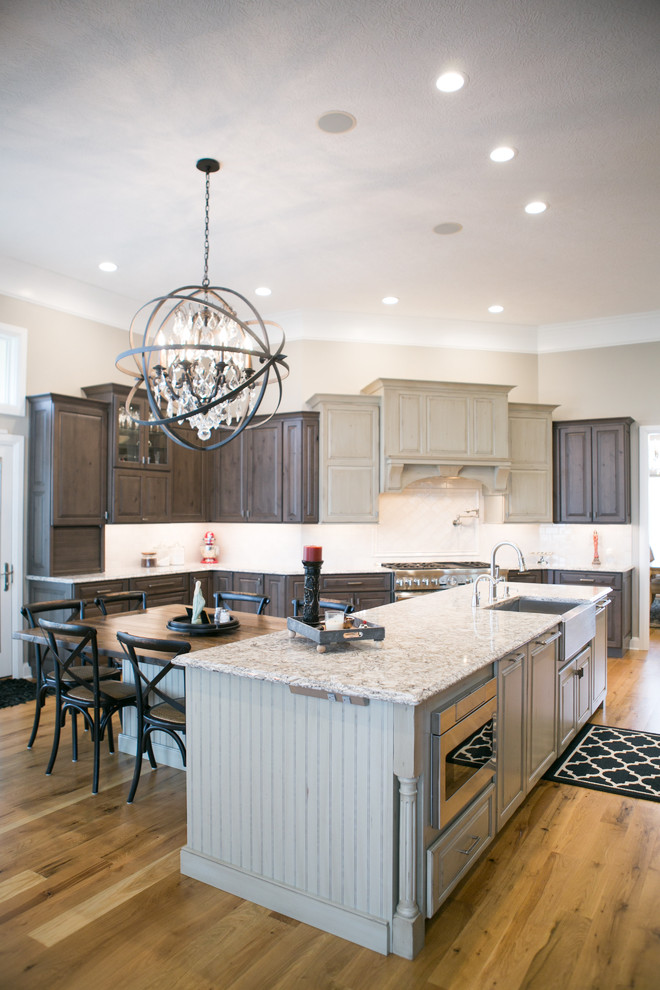 Example of a large transitional u-shaped medium tone wood floor and brown floor kitchen design in Indianapolis with a farmhouse sink, raised-panel cabinets, dark wood cabinets, granite countertops, white backsplash, subway tile backsplash, paneled appliances, an island and multicolored countertops