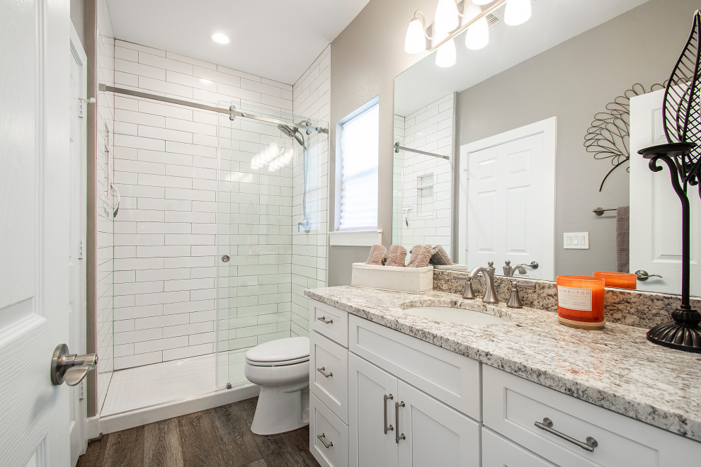 This is an example of a mid-sized transitional kids bathroom in Dallas with flat-panel cabinets, white cabinets, a double shower, a two-piece toilet, white tile, cement tile, grey walls, vinyl floors, an undermount sink, quartzite benchtops, brown floor, a sliding shower screen, grey benchtops, a single vanity and a built-in vanity.