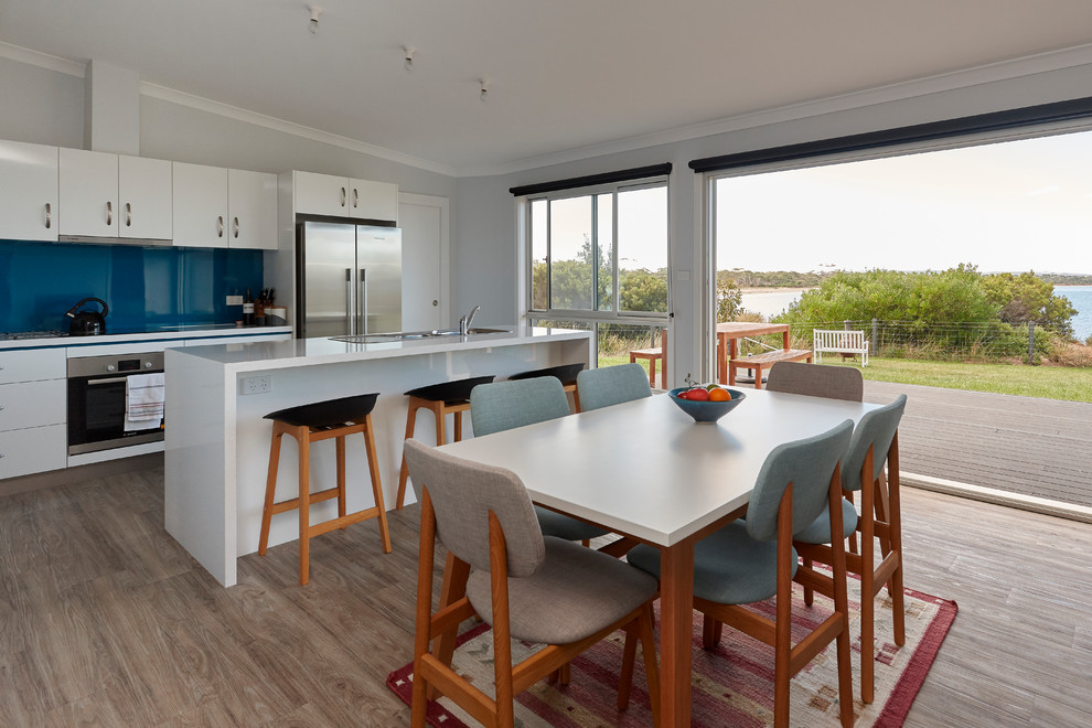 Design ideas for a contemporary galley eat-in kitchen in Other with a drop-in sink, flat-panel cabinets, white cabinets, blue splashback, glass sheet splashback, stainless steel appliances, medium hardwood floors, with island, brown floor and white benchtop.