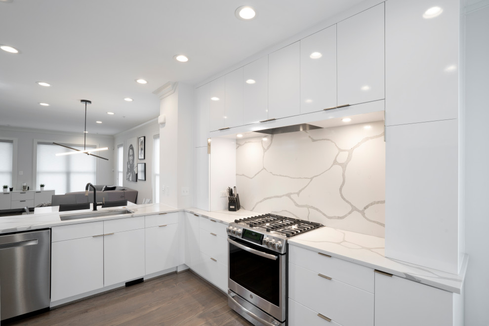 Inspiration for a mid-sized modern l-shaped open plan kitchen in DC Metro with a single-bowl sink, flat-panel cabinets, white cabinets, quartz benchtops, white splashback, engineered quartz splashback, stainless steel appliances, medium hardwood floors, a peninsula, grey floor and white benchtop.