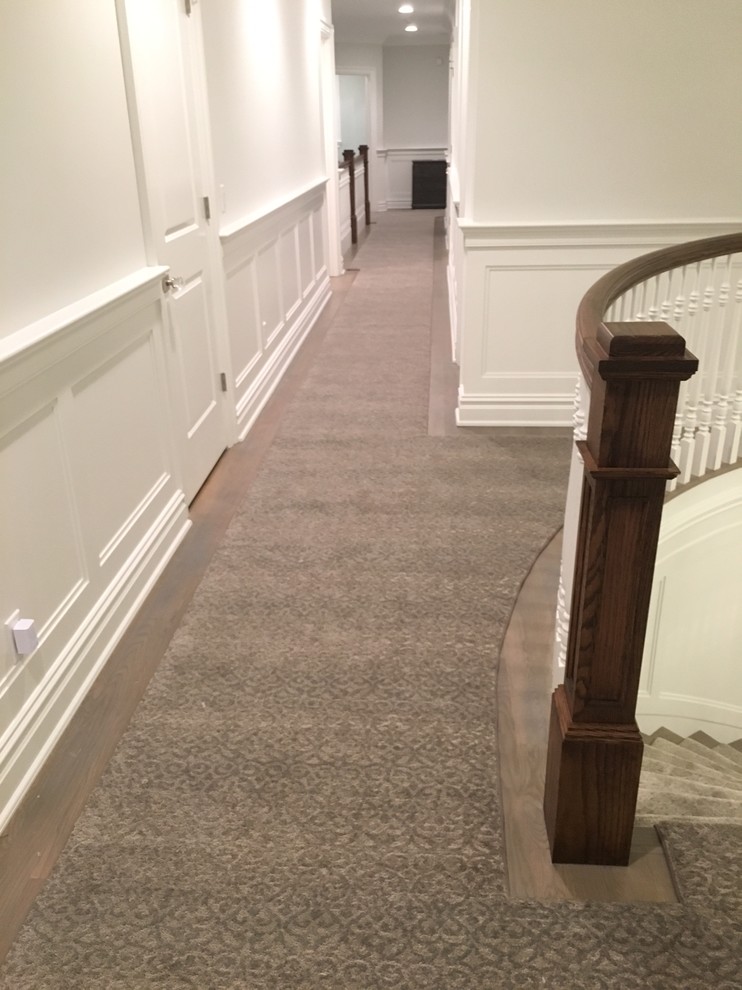 This is an example of an expansive traditional carpeted curved staircase in New York with carpet risers and wood railing.