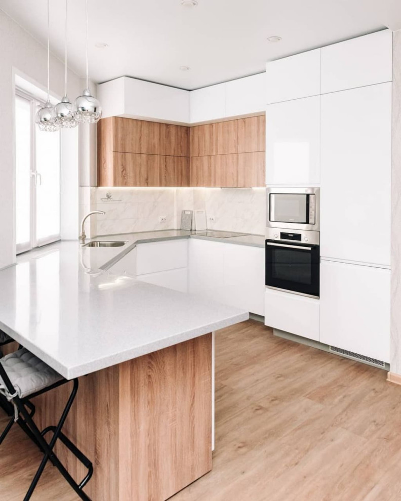 Large contemporary u-shaped kitchen/diner in Novosibirsk with a submerged sink, flat-panel cabinets, white cabinets, composite countertops, white splashback, glass sheet splashback, stainless steel appliances, medium hardwood flooring, a breakfast bar, brown floors and grey worktops.