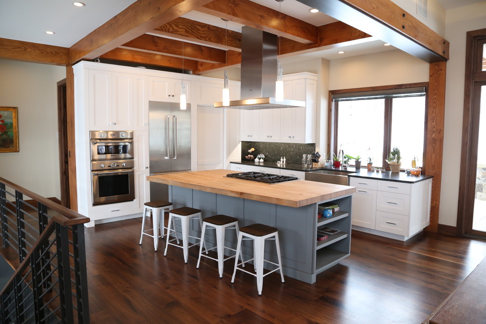 Mid-sized modern l-shaped open plan kitchen in Denver with a farmhouse sink, shaker cabinets, white cabinets, wood benchtops, stainless steel appliances, medium hardwood floors and with island.