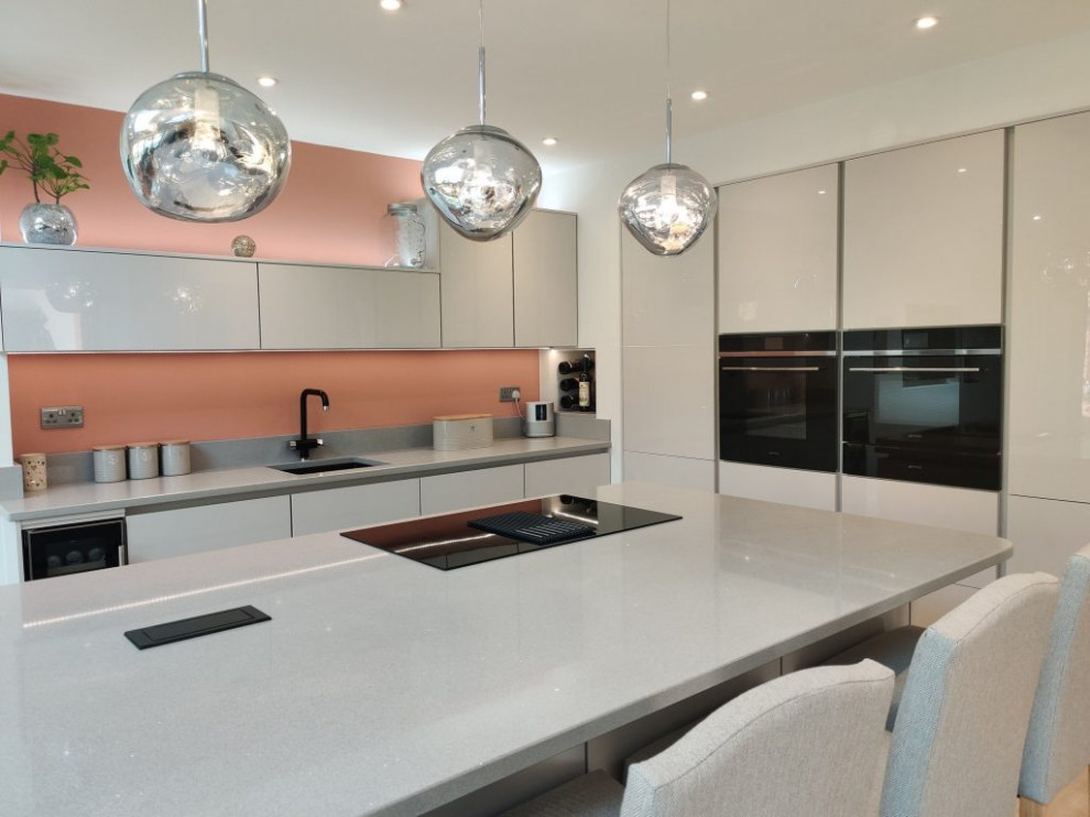 На фото: кухня-гостиная среднего размера: освещение в стиле модернизм с накладной мойкой, серыми фасадами, розовым фартуком, цветной техникой, островом и серой столешницей