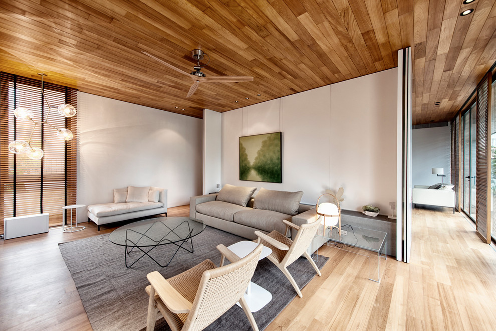 This is an example of a contemporary open concept living room in Singapore with white walls and light hardwood floors.