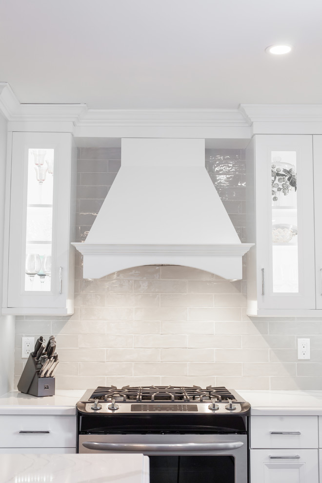 Large transitional l-shaped medium tone wood floor and brown floor enclosed kitchen photo with an undermount sink, recessed-panel cabinets, white cabinets, quartz countertops, gray backsplash, ceramic backsplash, stainless steel appliances, an island and white countertops