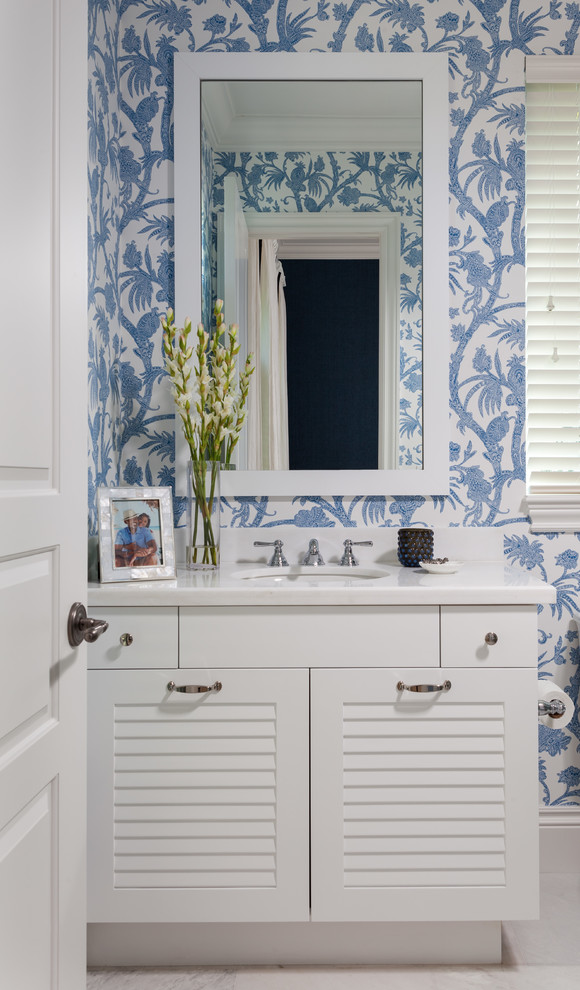 Photo of a beach style powder room in Miami with louvered cabinets, white cabinets, blue walls, an undermount sink and white benchtops.