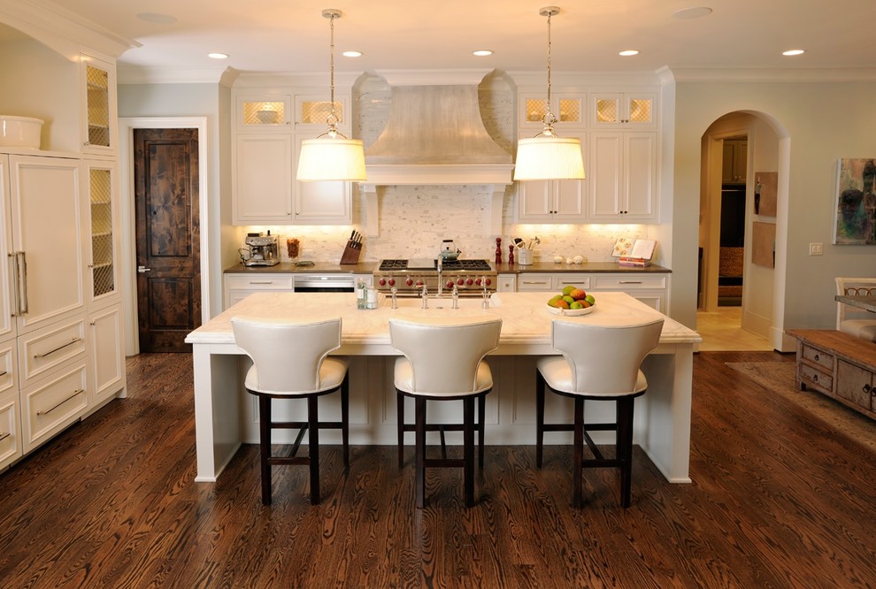 Mid-sized traditional single-wall eat-in kitchen in Nashville with white cabinets, panelled appliances, recessed-panel cabinets, marble benchtops, with island, a farmhouse sink, white splashback, stone tile splashback and dark hardwood floors.