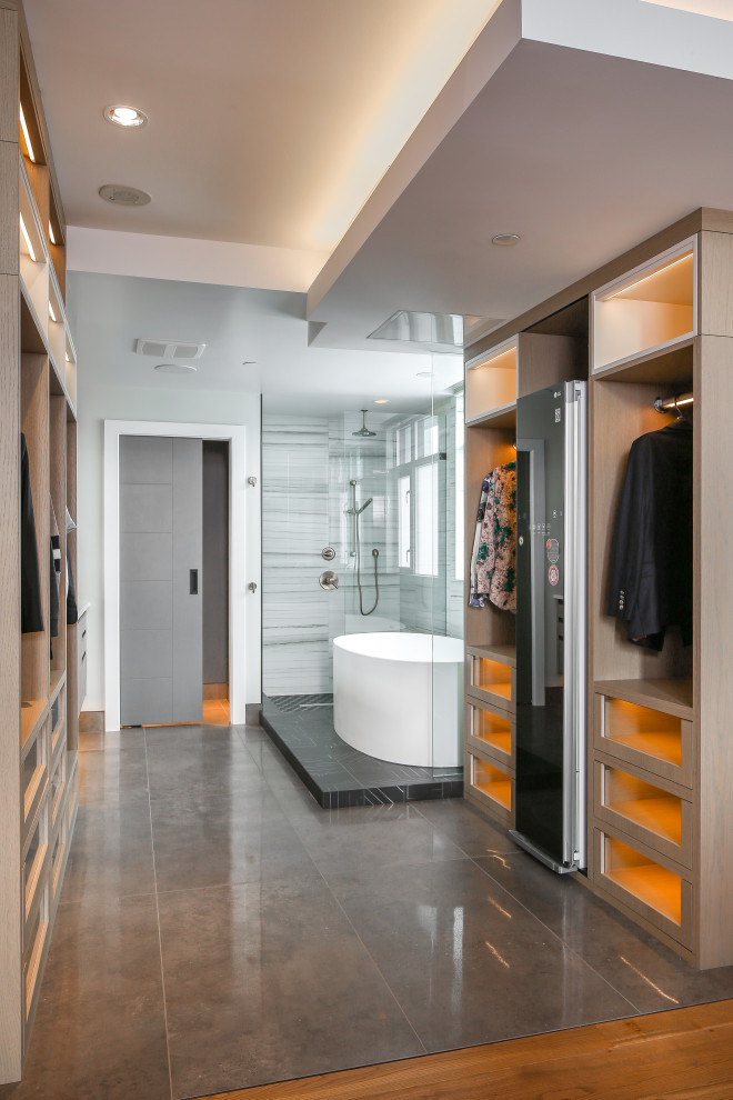 Expansive contemporary gender-neutral walk-in wardrobe in Vancouver with glass-front cabinets, light wood cabinets, concrete floors and black floor.