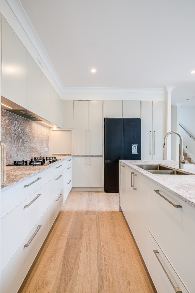 Inspiration for a large modern l-shaped open plan kitchen in Brisbane with a double-bowl sink, raised-panel cabinets, grey cabinets, quartz benchtops, engineered quartz splashback, black appliances, light hardwood floors, with island and brown floor.
