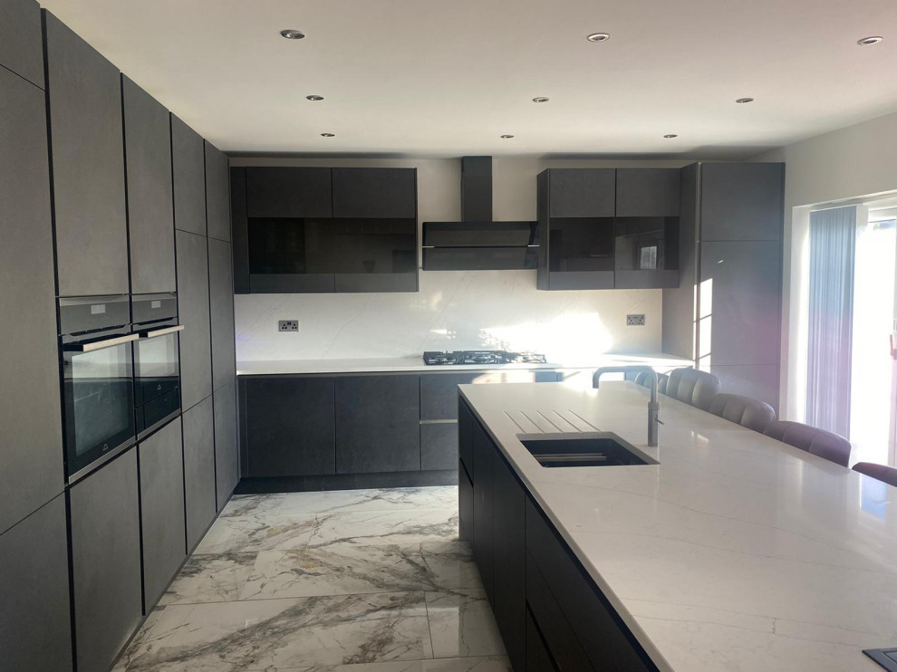 Photo of a large contemporary l-shaped eat-in kitchen in Cheshire with a drop-in sink, flat-panel cabinets, grey cabinets, quartzite benchtops, white splashback, engineered quartz splashback, black appliances, ceramic floors, with island, white floor and white benchtop.