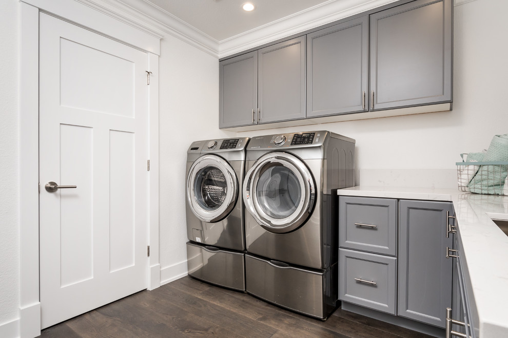 This is an example of a mid-sized modern l-shaped dedicated laundry room in San Francisco with an undermount sink, shaker cabinets, blue cabinets, quartz benchtops, white walls, laminate floors, a side-by-side washer and dryer and brown floor.