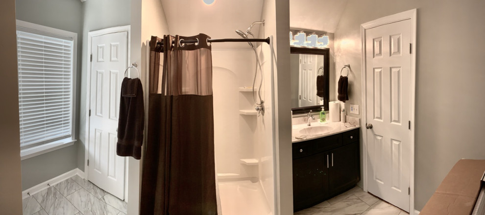 Example of a mid-sized trendy 3/4 porcelain tile, gray floor, single-sink and vaulted ceiling doorless shower design with raised-panel cabinets, brown cabinets, a two-piece toilet, gray walls, an integrated sink, marble countertops, gray countertops and a freestanding vanity