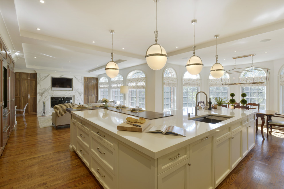Inspiration for a large transitional l-shaped medium tone wood floor and brown floor open concept kitchen remodel in New York with an undermount sink, shaker cabinets, white cabinets, quartzite countertops, white backsplash, marble backsplash, paneled appliances and an island