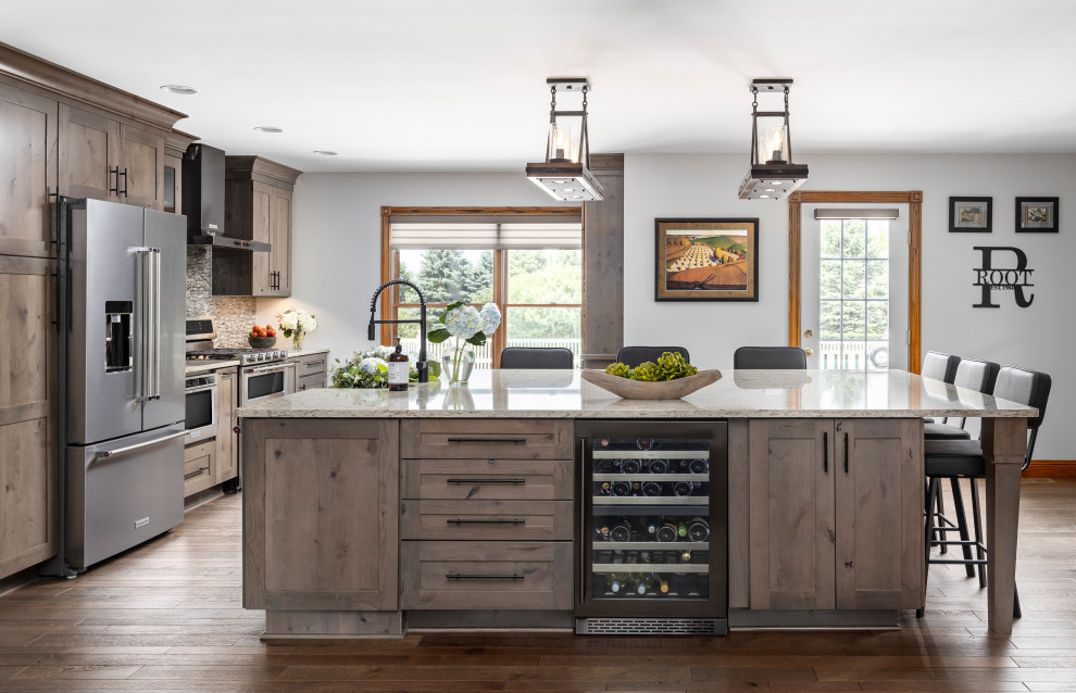 Mid-sized country single-wall open plan kitchen in Detroit with a farmhouse sink, shaker cabinets, grey cabinets, quartz benchtops, multi-coloured splashback, glass tile splashback, black appliances, medium hardwood floors, with island, grey floor and beige benchtop.