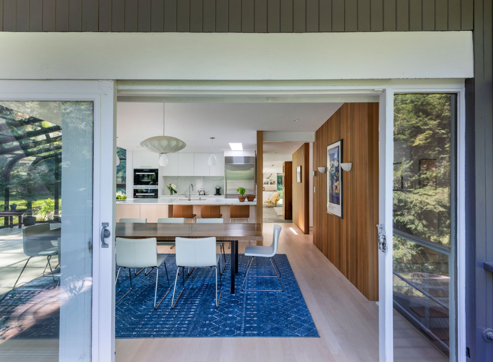 Immagine di una sala da pranzo aperta verso la cucina moderna con pareti bianche, parquet chiaro, pavimento beige e pareti in legno
