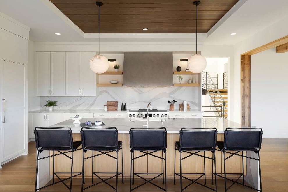 Photo of a country eat-in kitchen in Minneapolis with an undermount sink, flat-panel cabinets, white cabinets, quartz benchtops, white splashback, engineered quartz splashback, stainless steel appliances, light hardwood floors, with island, brown floor, white benchtop and timber.