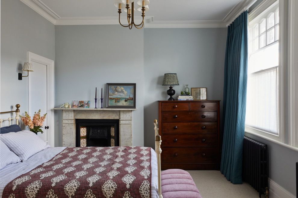 ロンドンにあるおしゃれな客用寝室 (青い壁、カーペット敷き、標準型暖炉、石材の暖炉まわり、ベージュの床) のインテリア