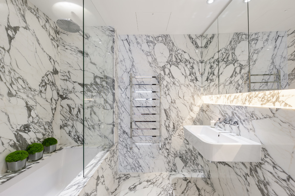 Mid-sized transitional master bathroom in London with a wall-mount sink, glass-front cabinets, grey cabinets, marble benchtops, an undermount tub, a shower/bathtub combo, a one-piece toilet, gray tile, stone slab, white walls and marble floors.