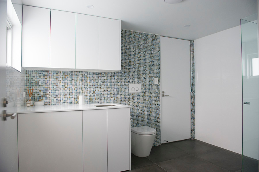 Inspiration for a mid-sized contemporary bathroom in Sydney with furniture-like cabinets, white cabinets, a corner shower, a wall-mount toilet, multi-coloured tile, mosaic tile, multi-coloured walls, porcelain floors, an undermount sink, engineered quartz benchtops, grey floor, a hinged shower door and white benchtops.