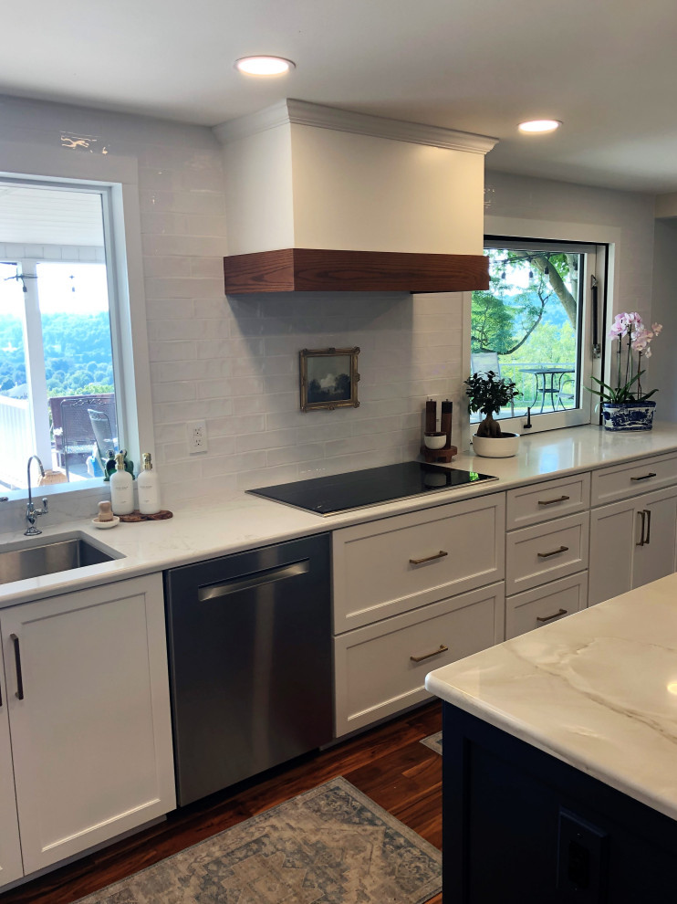Example of a mid-sized transitional l-shaped medium tone wood floor and brown floor kitchen pantry design with an undermount sink, flat-panel cabinets, blue cabinets, quartz countertops, white backsplash, subway tile backsplash, stainless steel appliances, an island and gray countertops
