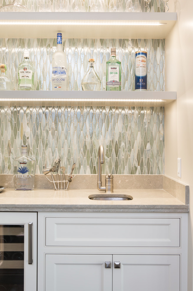 Photo of a small traditional single-wall wet bar in Los Angeles with shaker cabinets, white cabinets, limestone benchtops, an undermount sink, green splashback, medium hardwood floors and mosaic tile splashback.