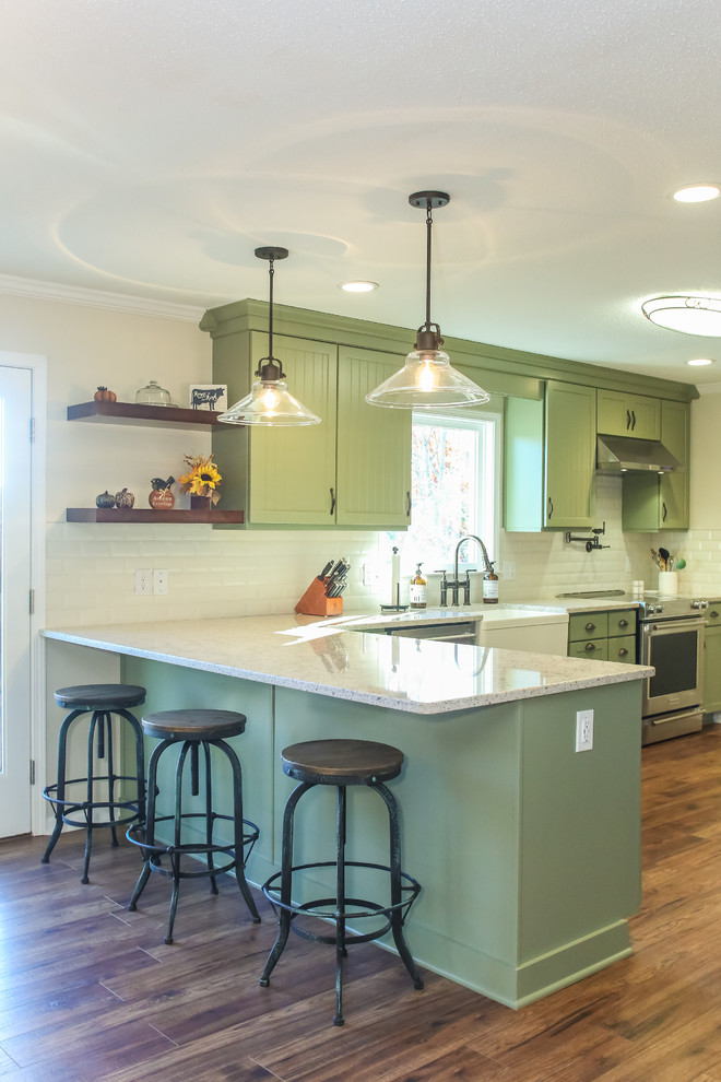 Mid-sized transitional l-shaped eat-in kitchen in Atlanta with a farmhouse sink, beaded inset cabinets, green cabinets, quartz benchtops, white splashback, subway tile splashback, stainless steel appliances, medium hardwood floors, a peninsula, brown floor and multi-coloured benchtop.