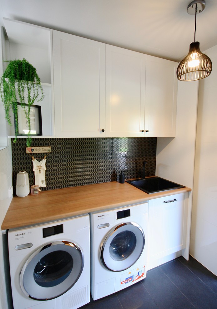 Small traditional single-wall dedicated laundry room in Sydney with a drop-in sink, shaker cabinets, white cabinets, wood benchtops, white walls, ceramic floors, a side-by-side washer and dryer and black floor.