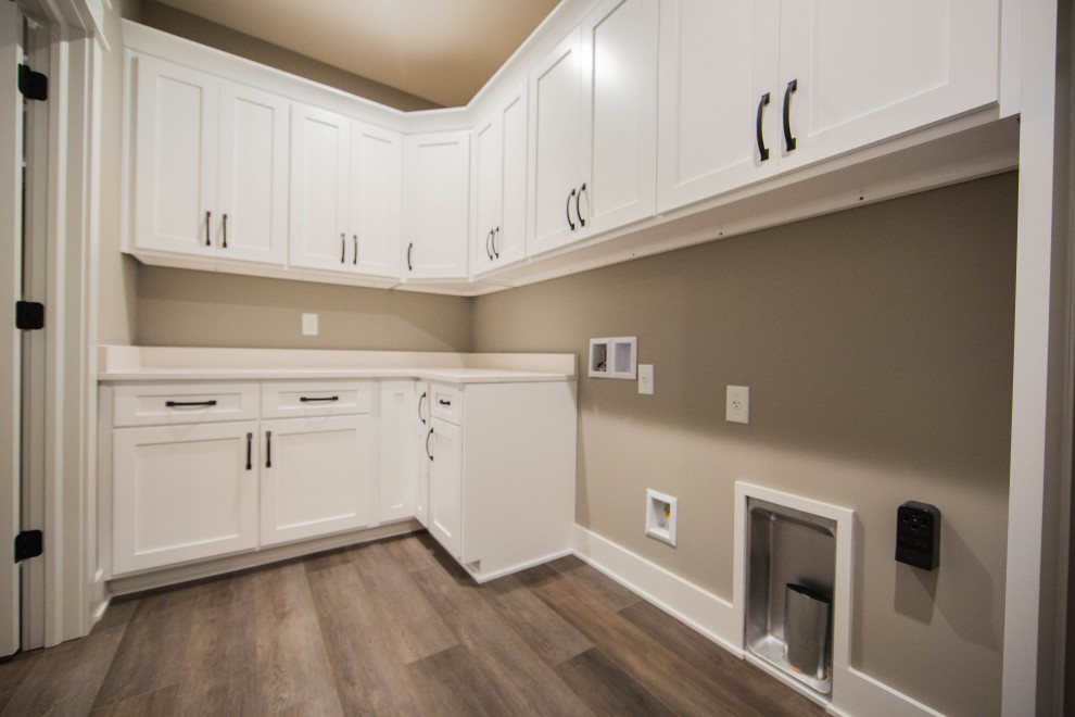 Photo of a mid-sized transitional l-shaped dedicated laundry room in Indianapolis with recessed-panel cabinets, white cabinets, quartz benchtops, brown walls, laminate floors, a side-by-side washer and dryer, brown floor and beige benchtop.