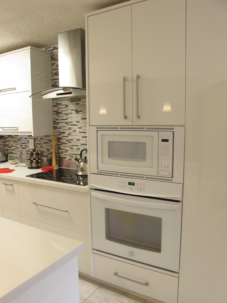 Mid-sized modern galley eat-in kitchen in Miami with a double-bowl sink, flat-panel cabinets, white cabinets, quartz benchtops, multi-coloured splashback, glass sheet splashback, white appliances, porcelain floors and a peninsula.