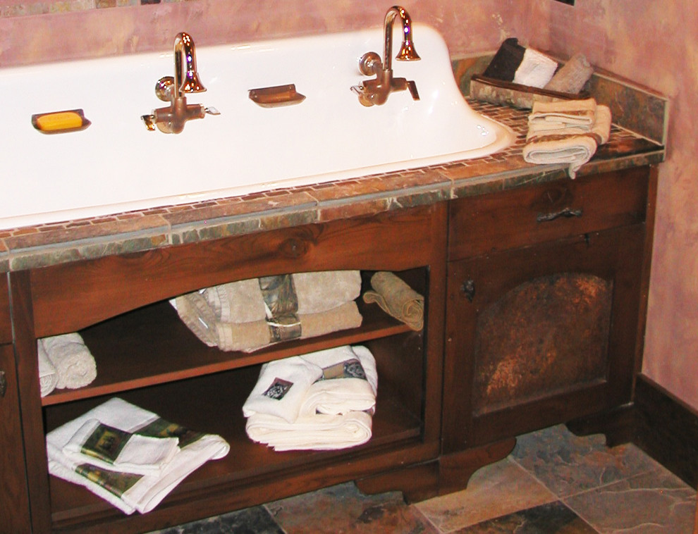 Photo of a mid-sized country 3/4 bathroom in Other with shaker cabinets, medium wood cabinets, beige tile, brown tile, gray tile, red walls, a drop-in sink, tile benchtops, slate floors and beige floor.