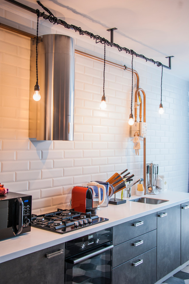 Inspiration for a small industrial single-wall open plan kitchen in Moscow with an undermount sink, flat-panel cabinets, grey cabinets, solid surface benchtops, white splashback, subway tile splashback, black appliances, porcelain floors, with island, grey floor and white benchtop.