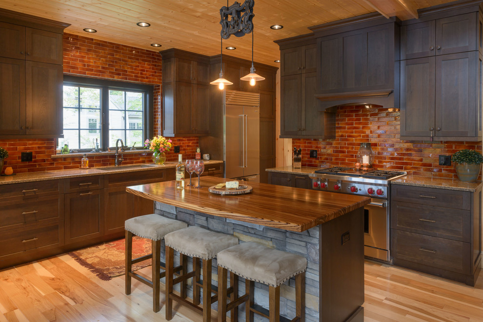 This is an example of a mid-sized country l-shaped open plan kitchen in Boston with an undermount sink, shaker cabinets, dark wood cabinets, stainless steel appliances, light hardwood floors, with island, granite benchtops, brown splashback, brick splashback and beige floor.