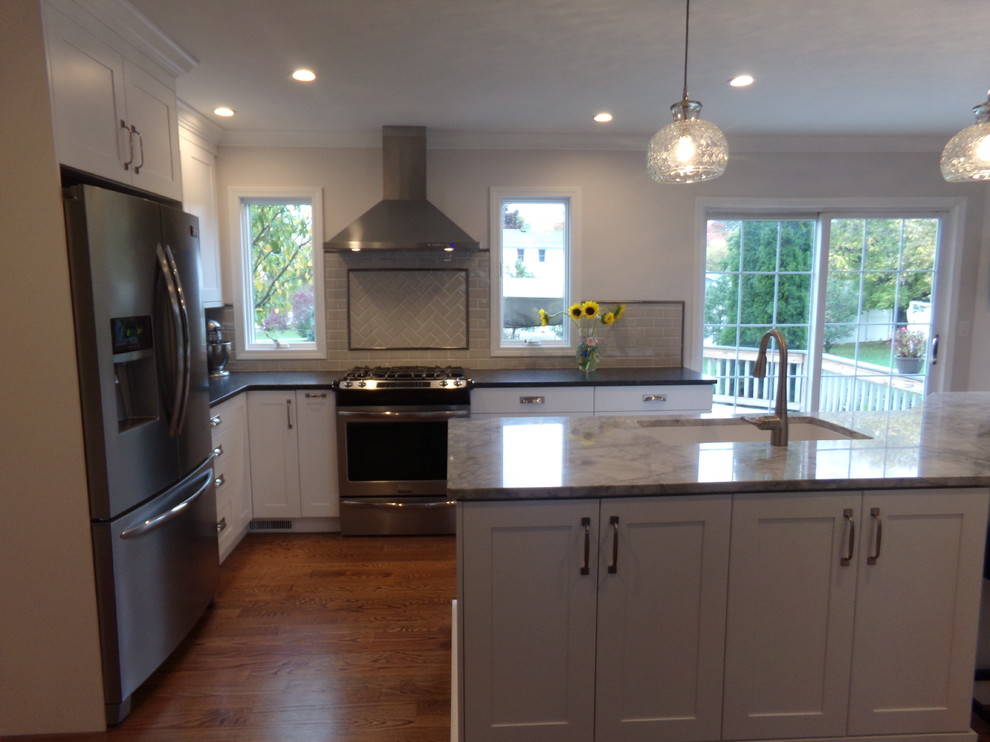 Mid-sized transitional l-shaped medium tone wood floor eat-in kitchen photo in New York with an undermount sink, recessed-panel cabinets, white cabinets, granite countertops, gray backsplash, ceramic backsplash, stainless steel appliances and an island