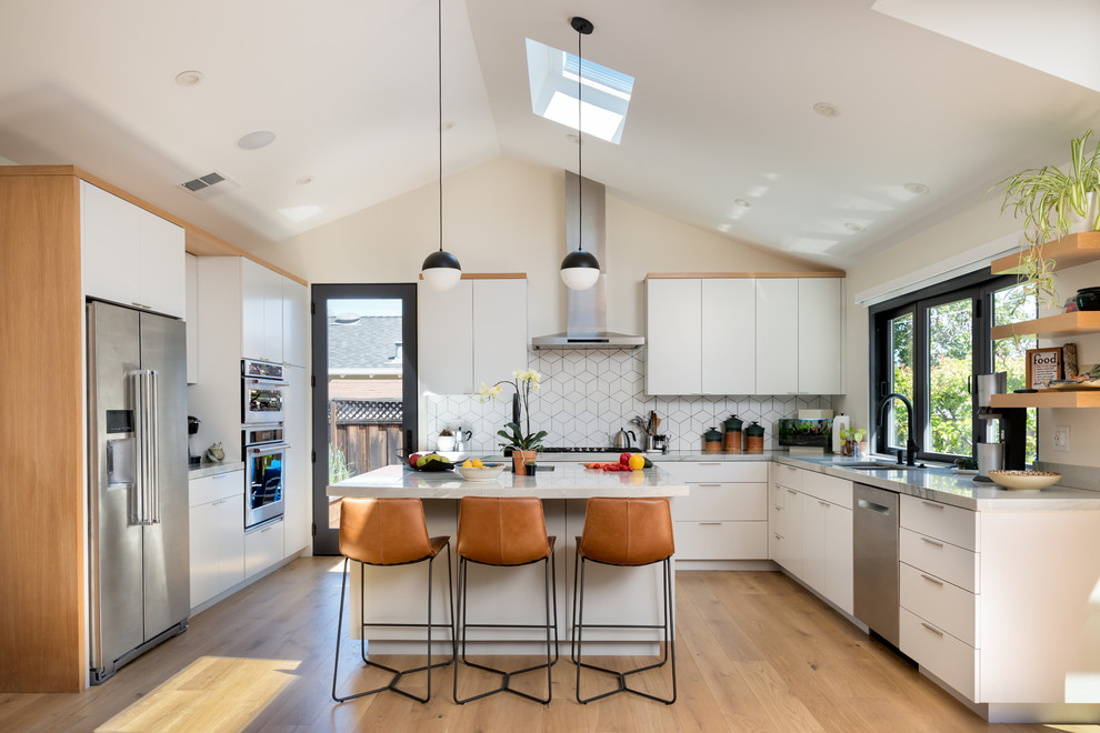 Photo of a contemporary kitchen in San Francisco with a double-bowl sink, flat-panel cabinets, white cabinets, white splashback, stainless steel appliances, medium hardwood floors, with island, brown floor and white benchtop.