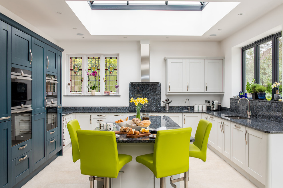 Mid-sized contemporary u-shaped open plan kitchen in Surrey with a single-bowl sink, recessed-panel cabinets, blue cabinets, granite benchtops, panelled appliances, ceramic floors, with island, beige floor and blue benchtop.