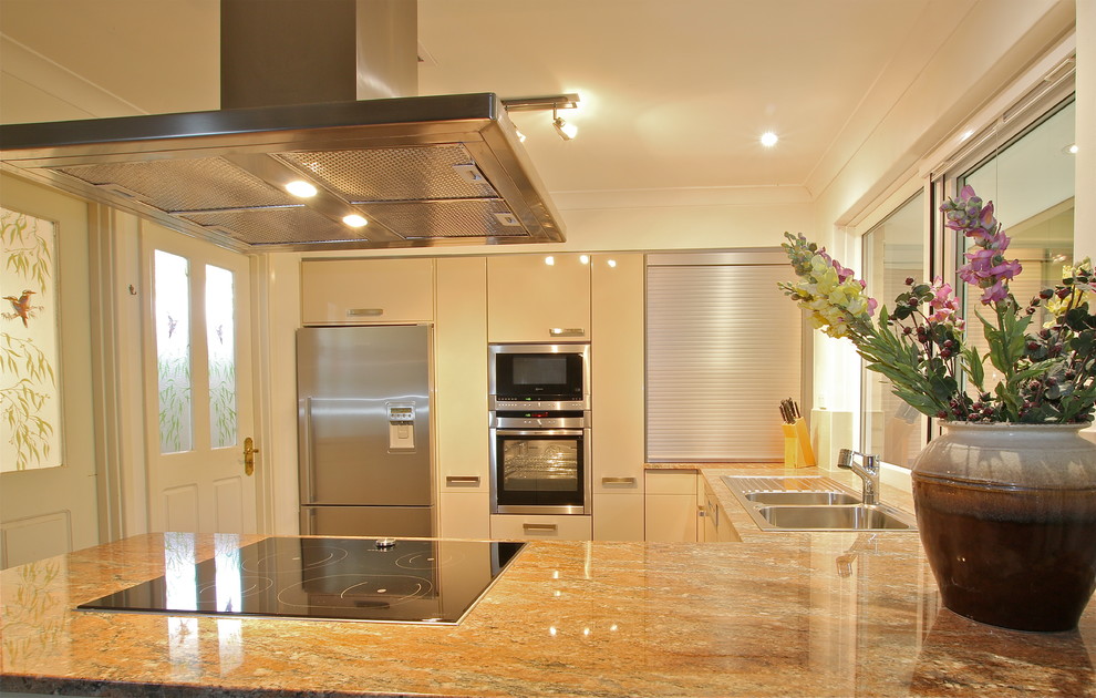 Photo of a mid-sized mediterranean u-shaped eat-in kitchen in Perth with a double-bowl sink, flat-panel cabinets, beige cabinets, granite benchtops, ceramic splashback, stainless steel appliances and ceramic floors.