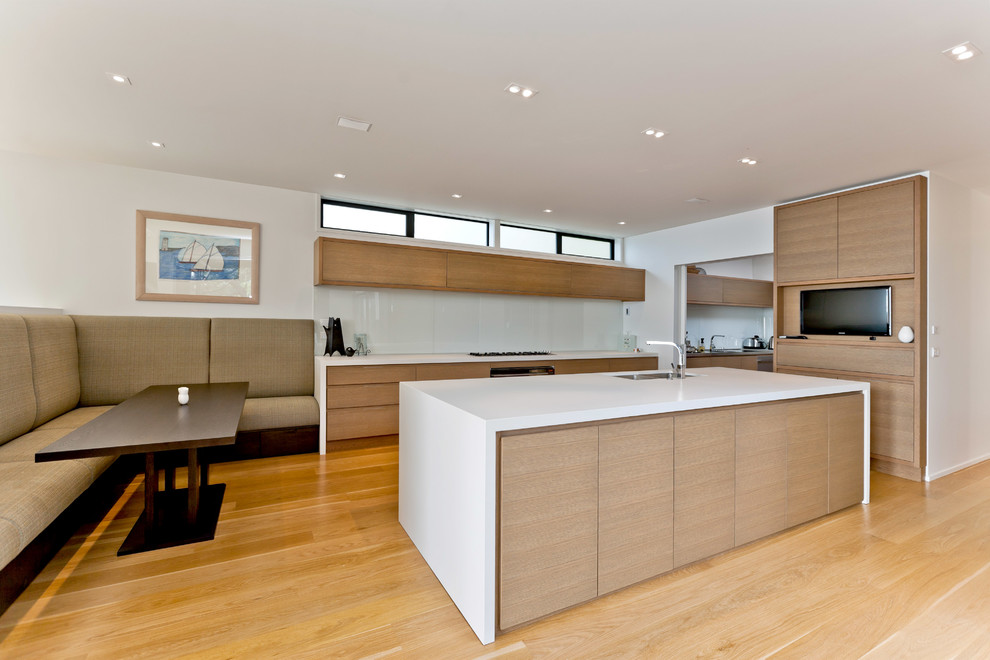 This is an example of a large contemporary l-shaped open plan kitchen in Auckland with an undermount sink, flat-panel cabinets, dark wood cabinets, granite benchtops, beige splashback, ceramic splashback, black appliances, light hardwood floors and with island.