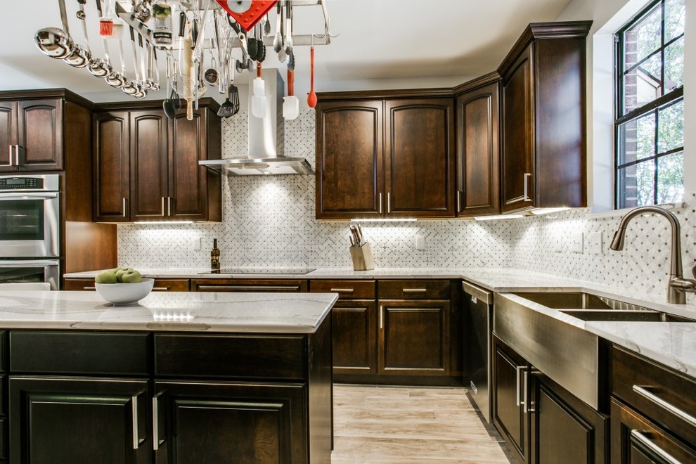 Enclosed kitchen - mid-sized transitional u-shaped light wood floor and beige floor enclosed kitchen idea in Dallas with a farmhouse sink, raised-panel cabinets, dark wood cabinets, quartzite countertops, white backsplash, ceramic backsplash, stainless steel appliances and an island
