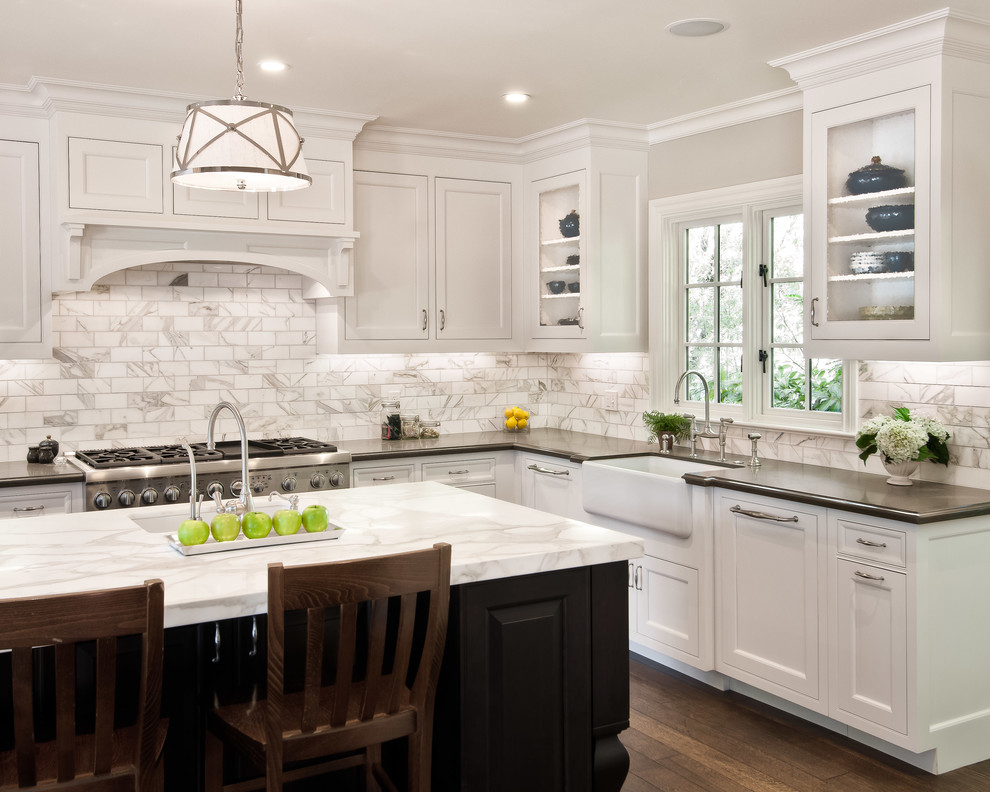Traditional l-shaped kitchen in San Francisco with a farmhouse sink, recessed-panel cabinets, white cabinets, white splashback, stainless steel appliances, dark hardwood floors, with island and stone tile splashback.