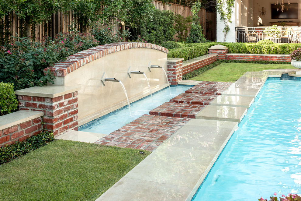 This is an example of a mid-sized traditional backyard custom-shaped pool in Houston with a water feature and brick pavers.