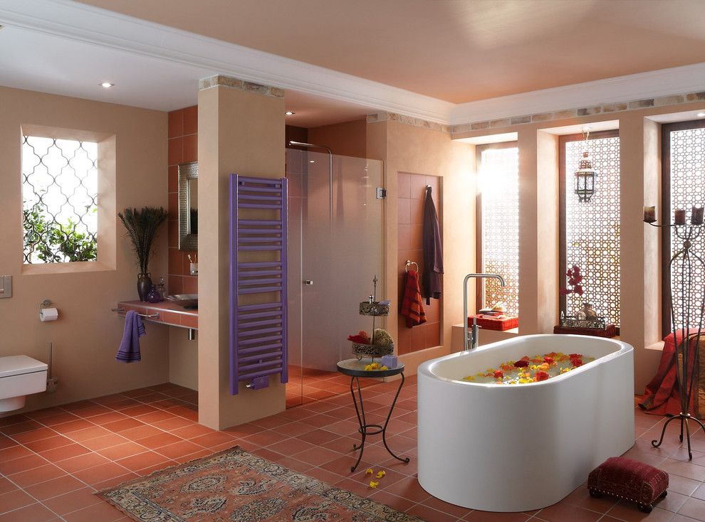 This is an example of an eclectic master bathroom in New York with a freestanding tub, an alcove shower, a wall-mount toilet, brown tile, stone tile, beige walls, terra-cotta floors and a vessel sink.