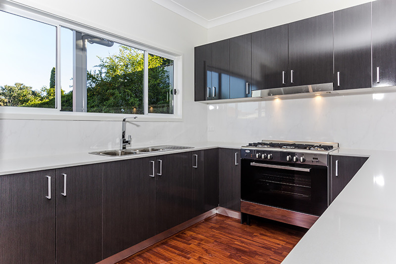 Mid-sized contemporary u-shaped kitchen pantry with a drop-in sink, flat-panel cabinets, dark wood cabinets, laminate benchtops, white splashback, ceramic splashback, stainless steel appliances, white walls, laminate floors and no island.